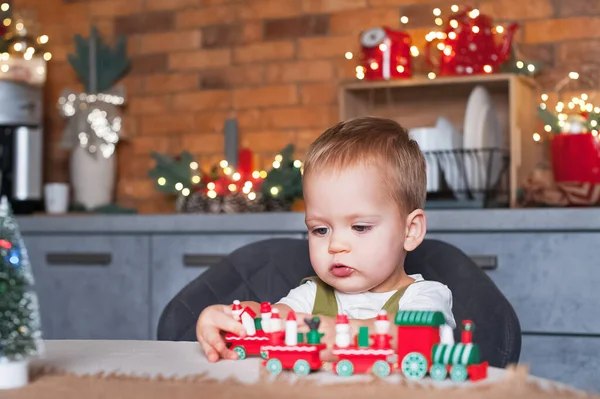 Cute toddler boy in pajamas with Christmas train at home close-up. New Years comfort at home, bedroom decor.