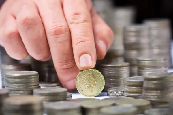 Primer plano de pila de monedas de libras británicas con una mano masculina — Foto de Stock