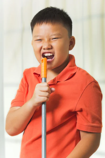 Giovane ragazzo asiatico tiene un manico di scopa come un microfono per cantare — Foto Stock