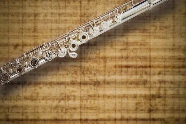 Professional silver flute on a an abstract music score background — Stock Photo, Image