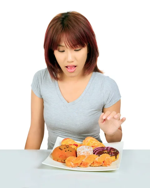 Isolated young asian woman with a donuts on the table — Stock Photo, Image