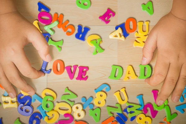 Mãos de um menino colocando "pai amor" alfabetos de plástico juntos . — Fotografia de Stock