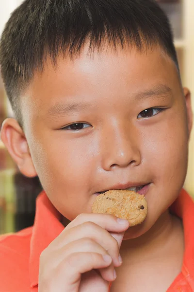 Giovane asiatico ragazzo mangia un pezzo di biscotto — Foto Stock