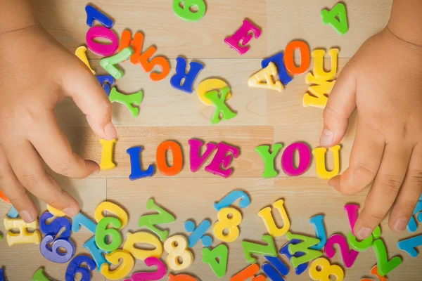 Handen van een jongen zetten -l love u-kunststof alfabetten samen. — Stockfoto