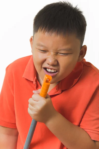 Young asian boy holds a broomstick as a microphone for singing — Stock Photo, Image