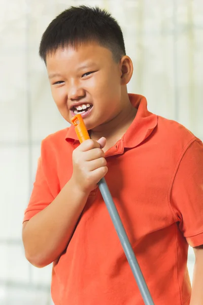 Giovane ragazzo asiatico tiene un manico di scopa come un microfono per cantare — Foto Stock