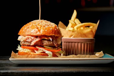 Salata, domates ve salatalık ile sulu sığır etli duble burger. Tabakta patates kızartması. Koyu arkaplan