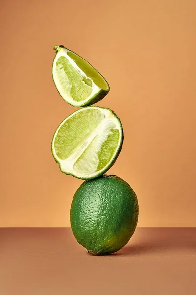Food balance and levitation. Whole and lime wedges stand one on one. Balance of fruits on a brown background.