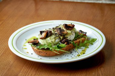Mantarlı avokado tostu ve ahşap arka planda beyaz bir tabakta haşlanmış yumurta.