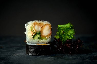 Koyu arkaplanda karides tempura, salatalık ve krem peynirli suşi rulosu. Yaklaş, seçici odaklanma