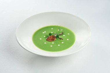 Beyaz bir masa örtüsü üzerinde beyaz bir tabakta istiridye ile kuşkonmaz kremalı çorba.