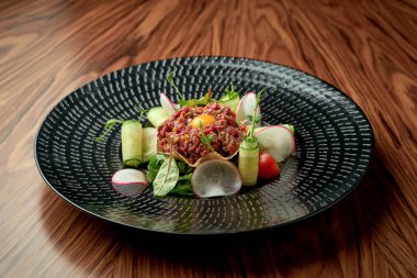 Tahta arka planda siyah bir tabakta sarısı olan iştah açıcı sığır etli tartar.