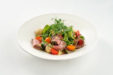 Beyaz tabakta biftek ve çam fıstığı ile salata..