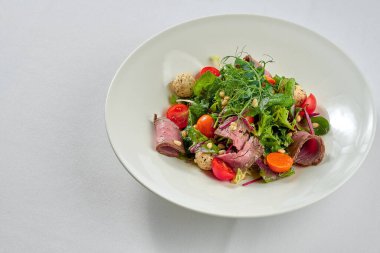 Beyaz tabakta biftek ve çam fıstığı ile salata..