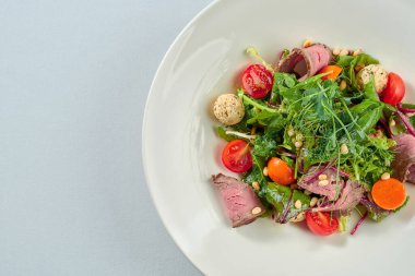 Beyaz tabakta biftek ve çam fıstığı ile salata..