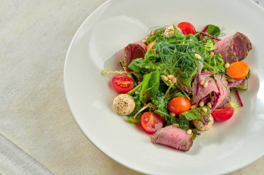 Beyaz tabakta biftek ve çam fıstığı ile salata..