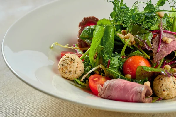 Beyaz tabakta biftek ve çam fıstığı ile salata..