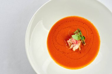 Beyaz masa örtüsünde beyaz bir tabakta yengeçli fırında domates çorbası.