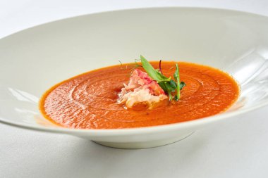 Beyaz masa örtüsünde beyaz bir tabakta yengeçli fırında domates çorbası.