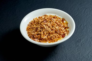 Sağlıklı kahvaltı - ballı granola ve siyah arka planda beyaz tabakta yoğurt