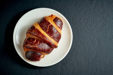 Siyah arka planda beyaz tabakta chockolate ile kremalı tatlı kruvasan.