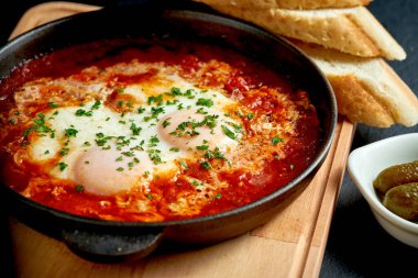 Kızarmış yumurta shakshuka domates soslu, siyah arka planda beyaz bir tabakta kızartma tavasında.