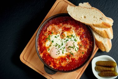 Kızarmış yumurta shakshuka domates soslu, siyah arka planda beyaz bir tabakta kızartma tavasında.