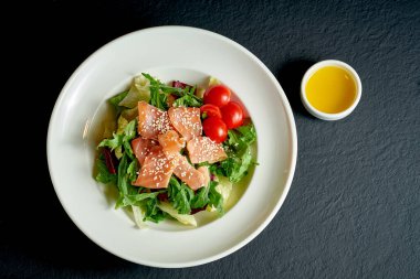 Siyah arka planda beyaz tabakta domatesli diyet salatası ve somon balığı.