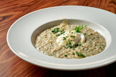 Parmesanlı yulaf ezmesi ve ahşap arka planda beyaz bir tabakta haşlanmış yumurta.