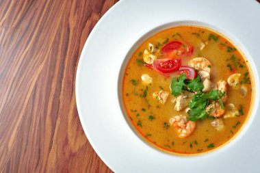 Karidesli Asya çorbası ve ahşap arka planda beyaz bir tabakta tavuk.