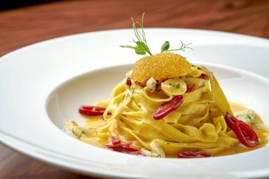 İtalyan Pepperoncini Makarnası, sarımsak, acı biber ve beyaz bir tabakta turna balığı havyarı ile ahşap arka planda.