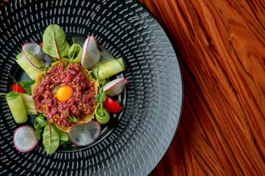 Tahta arka planda siyah bir tabakta sarısı olan iştah açıcı sığır etli tartar.