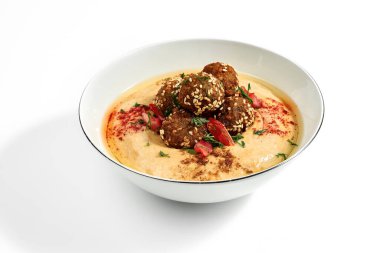 Hummus with olive oil, tomatoes and specials in a bowl on a white plate. Photo for the menu. Isolated