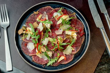 Beef carpaccio with capers, parmesan and truffle in a black plate. Selective focus, close-up. Noise grain in post-production