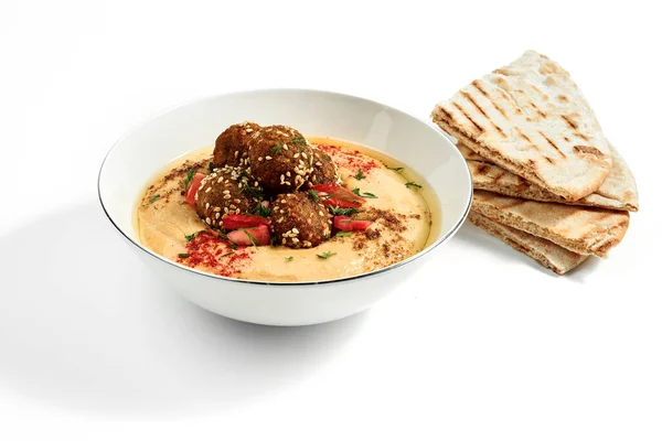 Hummus with olive oil, tomatoes and specials, pita in a bowl in a white plate. Photo for the menu. Isolated
