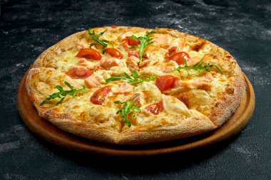 Pizza with salmon, tomatoes and arugula on a black stone background. 45 degree angle view. Close-up, selective focus
