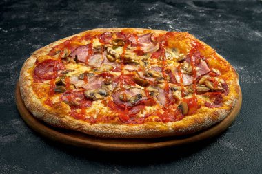 Pizza with bacon, salami and mushrooms on a black stone background. 45 degree angle view. Close-up, selective focus