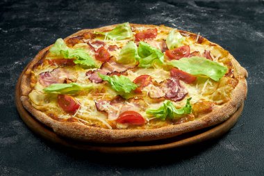Pizza with bacon, parmesan and lettuce on a black stone background. 45 degree angle view. Close-up, selective focus