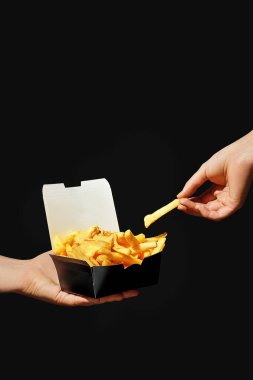 Elleri patates kızartmasını kara kutuda tutarken diğer eli patatesi sarı sosa batırıyor. Siyah arkaplan