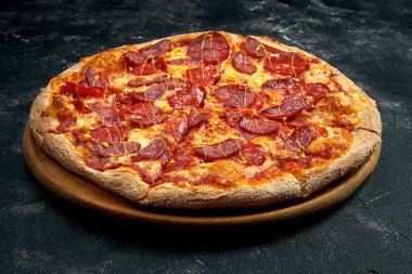 Pizza with salami and smoked sausages on a black stone background. 45 degree angle view. Close-up, selective focus