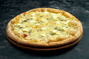 Pizza with 4 types of cheeses on a black stone background. 45 degree angle view. Close-up, selective focus