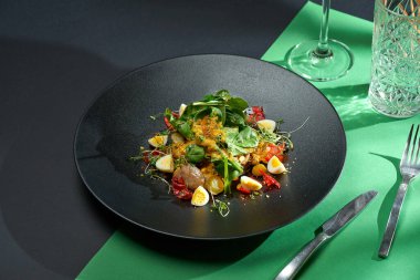 Salad with chicken liver, citrus confit and eggs in a black plate. Colored backgrounds. Hard light. selective focus