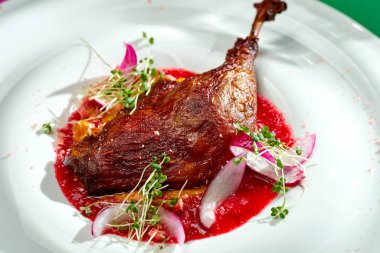 Ördek bacağı kırmızı sos ve parlak arkaplanda bir tabakta soğan karışımı. Seçici odak, sert gölgeler