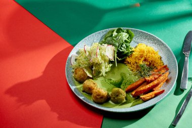 Yeşil soslu Hint köri pilavı, tatlı patates ve bir tabak dolusu köfte. Seçici odaklanma, sert ışık