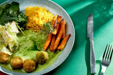 Yeşil soslu Hint köri pilavı, tatlı patates ve bir tabak dolusu köfte. Seçici odaklanma, sert ışık