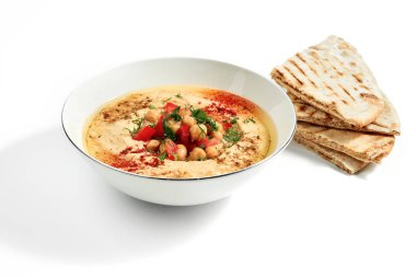 Baharatlı humus, nohut, domates ve pide ekmeği beyaz arka planda izole edilmiş bir kasede.