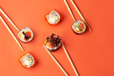 Somon ve yengeç karışımlı farklı suşi ruloları ve turuncu arka planda çubuklar.