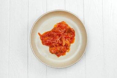 Kırmızı soslu balık yahnisi ve beyaz ahşap arka planda sebzeler.