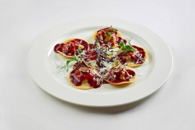 Soslu ve dana yanaklı Ravioli, beyaz masa örtüsünde parmesan peyniri.