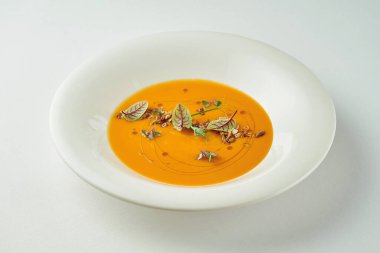 Beyaz masa örtüsü üzerinde beyaz bir tabakta balkabağı kremalı çorba.